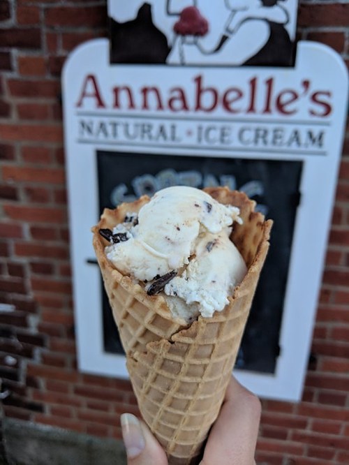 A hand holding a waffle cone filled with chocolate chip ice cream in front of Annabelle's Natural Ice Cream sign.