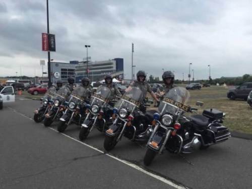 A row of state police motorcycles lined up, with officers standing beside them in uniform.