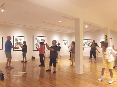 A group of people practicing movement in an art gallery, surrounded by black-and-white artwork on the walls.