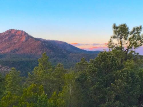 Scenic view of mountains and trees at sunset, with a clear blue sky and soft clouds in the background.
