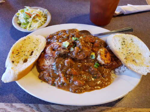 A plate of shrimp in a rich sauce, served with rice, two slices of garlic bread, and a side of coleslaw.
