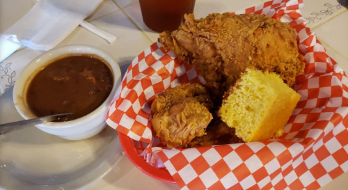 A plate with fried chicken, cornbread, and a bowl of beans, served in a red-checkered basket.