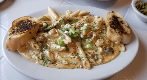 Creamy pasta with vegetables, topped with green onions, served with toasted garlic bread on the side.