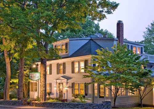 A charming inn surrounded by trees, featuring a welcoming facade with large windows and a sign that reads "Newcastle Inn."