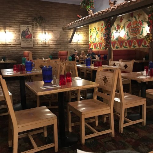 Cozy restaurant interior with wooden tables, colorful glassware, and decorative walls, featuring a few diners.