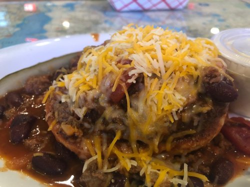 A hearty dish featuring a large, cheesy meat and bean topping on a crispy base, served with a side of sauce.