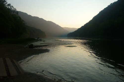 Serene river scene at dusk, with misty mountains and calm water reflecting the soft light.