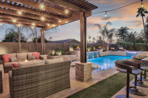 A stylish outdoor patio with a pool, cozy seating, and string lights, set against a sunset backdrop.