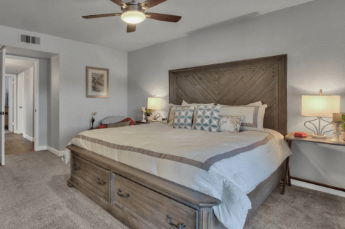 Cozy bedroom featuring a large bed with decorative pillows, nightstands, and a ceiling fan in a softly lit space.