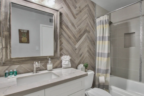 Modern bathroom featuring a herringbone tile wall, a large mirror, and a bathtub with a shower curtain.