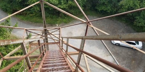 View from the top of a metal tower, looking down at a gravel path and a parked white car below.