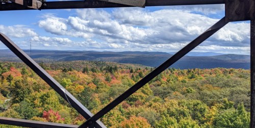 A scenic view of colorful autumn foliage and rolling hills under a partly cloudy sky, framed by a metal structure.