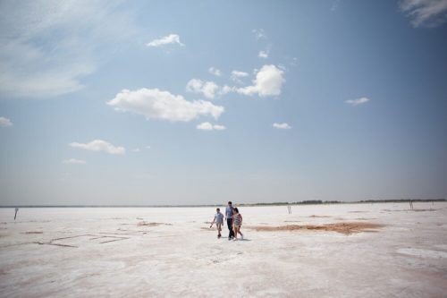 A group of people walking on a vast, white salt flat under a blue sky with scattered clouds.