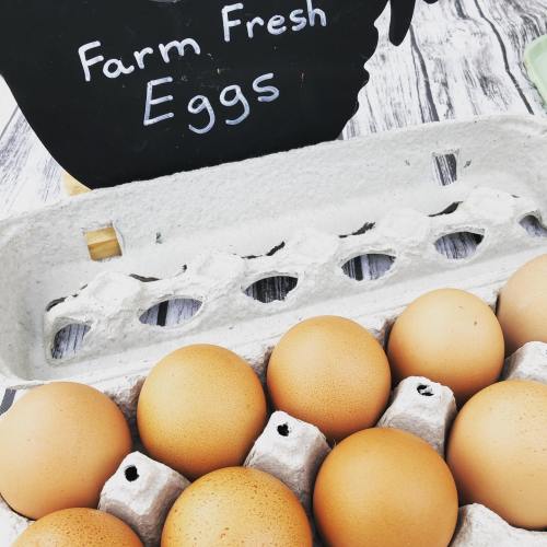 A carton of brown eggs sits on a wooden surface next to a sign that reads "Farm Fresh Eggs."