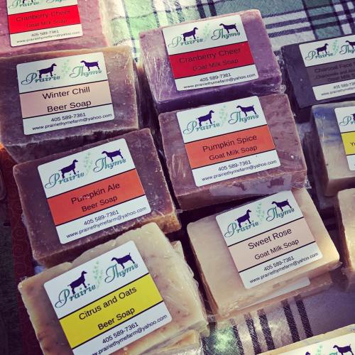 A variety of colorful handmade soaps with labels, displayed on a checkered tablecloth.