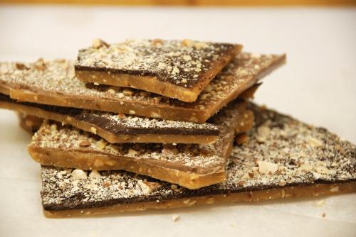 A stack of chocolate-covered toffee pieces sprinkled with crushed nuts on a white surface.