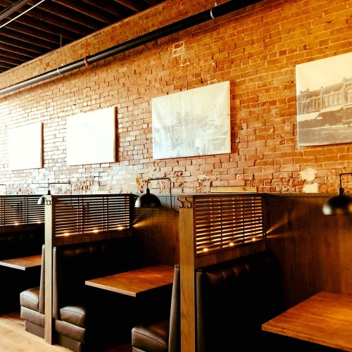 Cozy restaurant interior with wooden booths, exposed brick walls, and vintage photos hanging above.