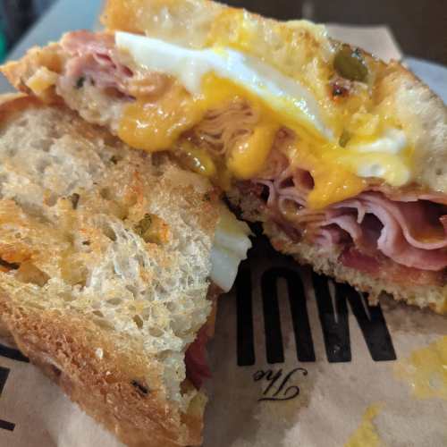 Close-up of a sandwich with layers of ham, cheese, and egg on toasted bread, cut in half and served on paper.