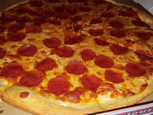 A close-up of a large pepperoni pizza with a golden crust and melted cheese, arranged in a pizza box.