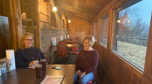 Two women sit at a wooden table in a cozy restaurant, enjoying drinks and chatting in a rustic setting.