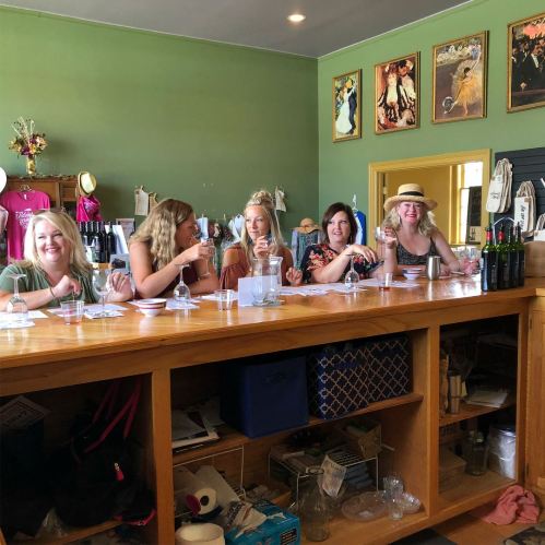 A group of five women enjoying drinks at a bar, surrounded by a vibrant green wall and decorative artwork.