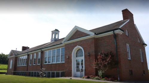 A brick building with large windows and a clock tower, surrounded by greenery and flowers.