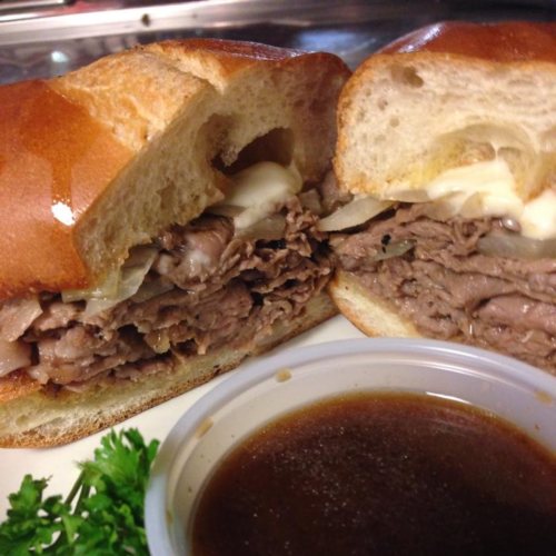 Close-up of a sliced sandwich filled with beef, onions, and mayonnaise, served with a side of dipping sauce.
