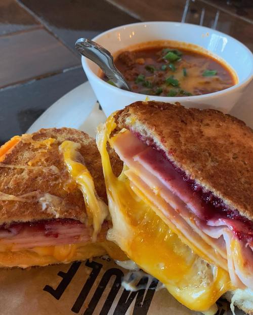 A grilled sandwich with melted cheese and ham, served with a bowl of chili topped with green onions.