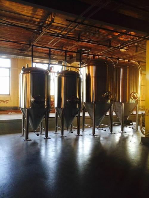 Four shiny stainless steel fermentation tanks in a well-lit industrial space.