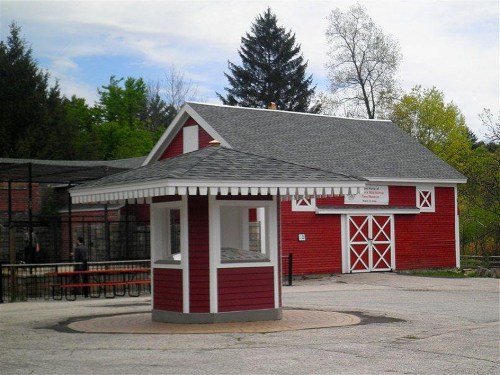 A red building with a white roof and trim, featuring a circular kiosk in front, surrounded by trees and a cloudy sky.
