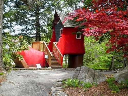 A whimsical red shoe-shaped house surrounded by trees and colorful foliage.