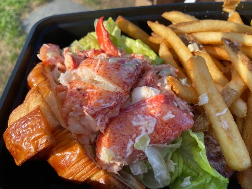 A lobster roll with chunks of lobster on lettuce, served in a croissant, alongside a portion of French fries.