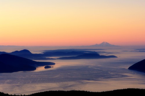 A serene landscape at sunset, featuring mountains and islands silhouetted against a colorful sky.