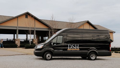 A black van with "DSH" on the side parked in front of a building with a wooden porch and gravel driveway.