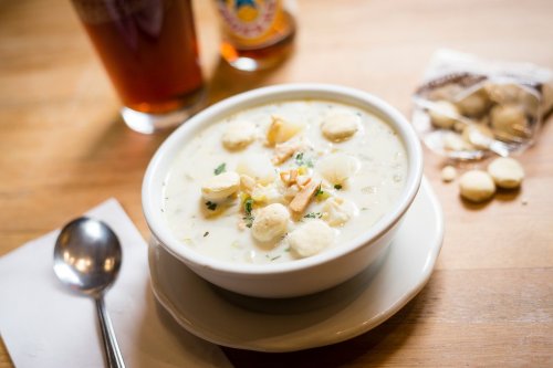 A bowl of creamy soup topped with crackers and herbs, accompanied by a spoon and a drink in the background.