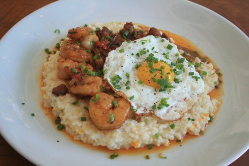 A plate of creamy grits topped with shrimp, sausage, and a sunny-side-up egg, garnished with green onions.