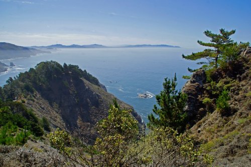 A scenic coastal view featuring cliffs, greenery, and a calm ocean under a clear blue sky.