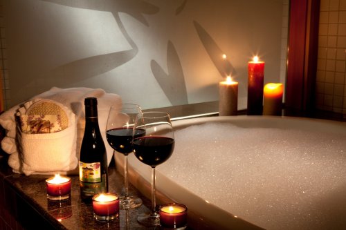 A cozy bathroom scene with a bubble-filled tub, candles, wine glasses, and a bottle of wine, creating a relaxing atmosphere.