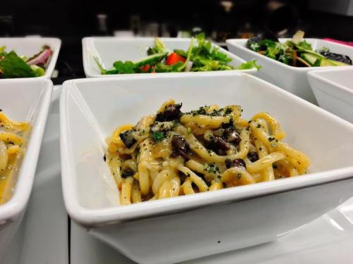 A bowl of pasta with a creamy sauce, garnished with herbs, alongside fresh salads in white dishes.
