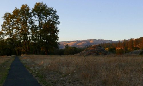 A serene landscape at sunset featuring a path, trees, and rolling hills in the background.