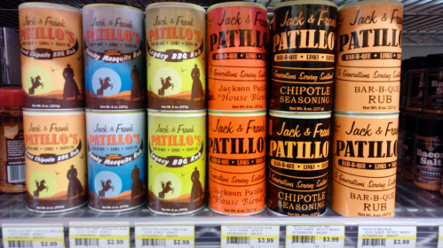 Cans of Patillo's BBQ seasonings in various flavors displayed on a store shelf.