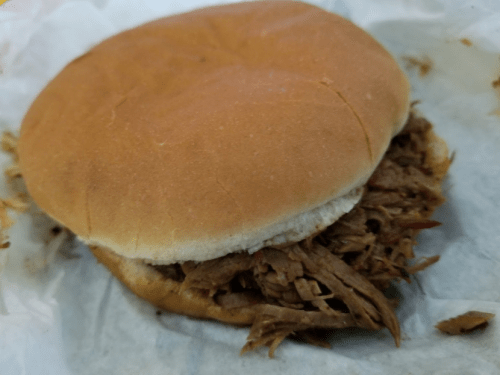 A pulled pork sandwich on a soft bun, served on white parchment paper.