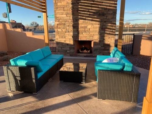 Outdoor seating area with turquoise couches and a stone fireplace, set against a clear sky.