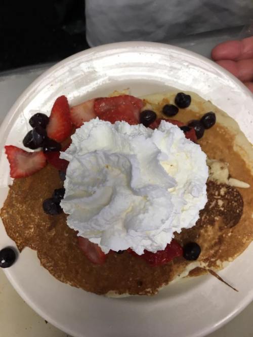 A plate of pancakes topped with whipped cream, strawberries, and blueberries.