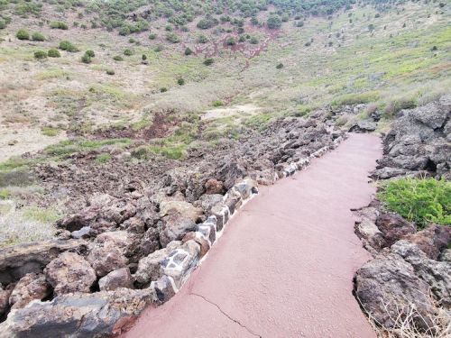 A winding path through rocky terrain, surrounded by green hills and sparse vegetation.