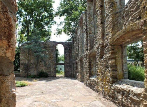 Ruins of a stone structure surrounded by trees, featuring an archway and a stone pathway.
