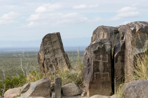 Rock formations with sparse vegetation overlook a vast landscape under a cloudy sky.