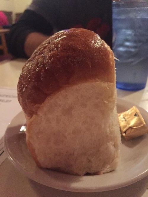 A golden-brown dinner roll on a small plate, with a butter packet beside it.