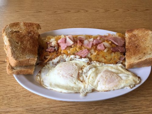 A plate with two fried eggs, hash browns topped with ham and onions, and two slices of toasted bread.