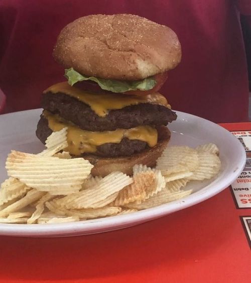 A stacked cheeseburger with lettuce and tomato on a plate, accompanied by a side of potato chips.